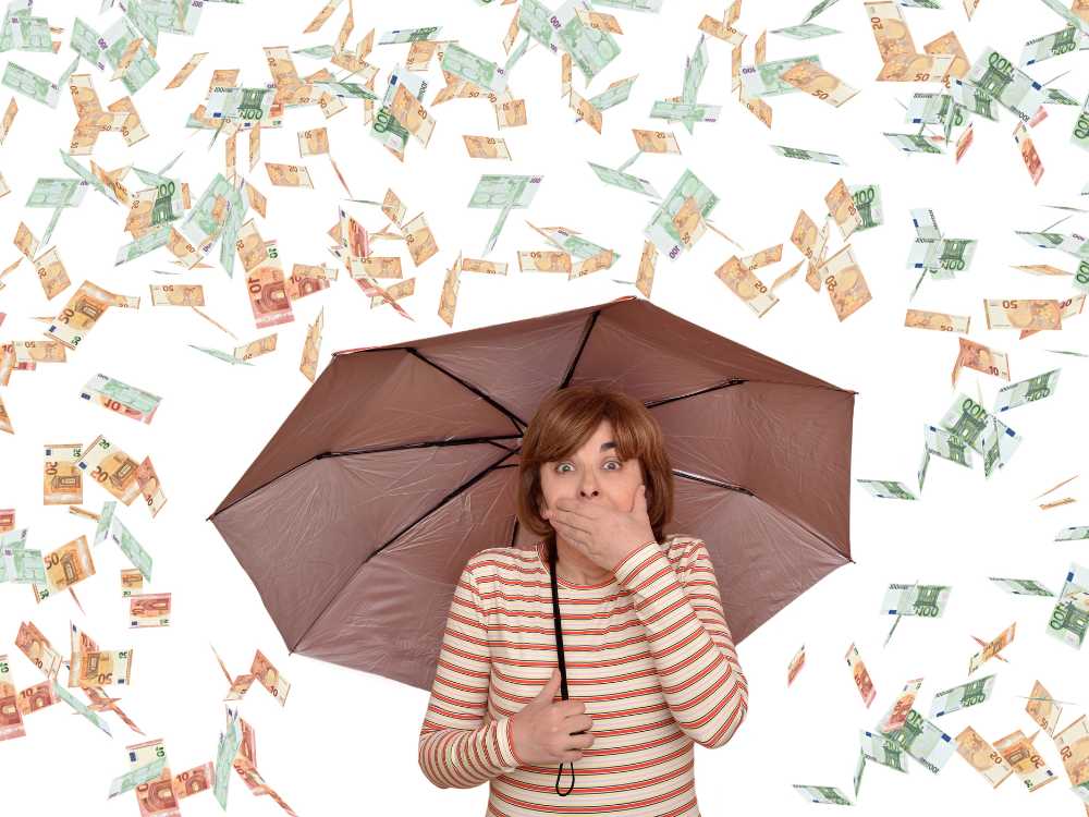 На удивленную девушку под зонтом сыпятся денежные купюры