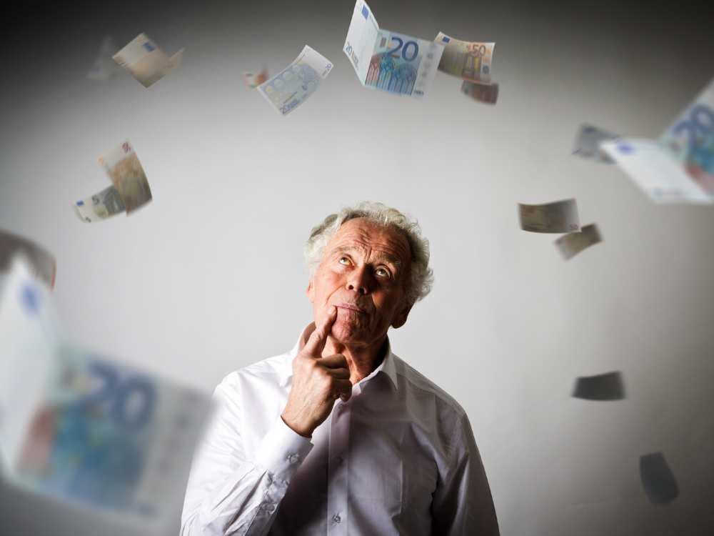 Пожилой мужчина задумчиво смотрит на падающие евро