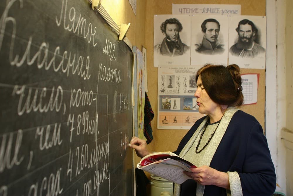 Учитель русского языка пишет на доске и объясняет материал