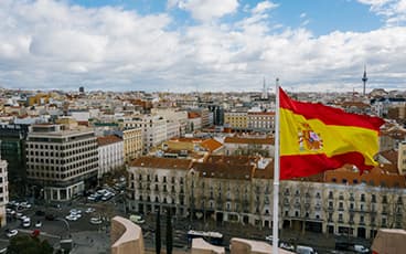 Испанский флаг развивается на фоне городских крыш